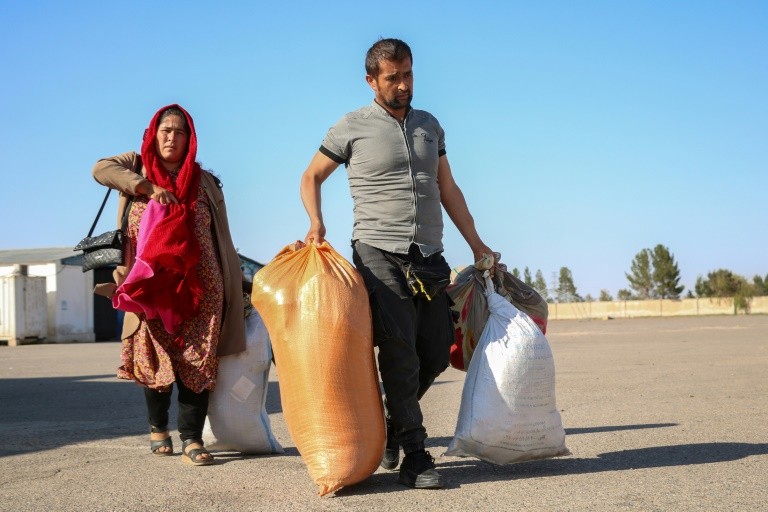 Afghan refugee Fazila Qaderi (L) and her husband carry their belongings after their deportation from Iran, at a registration centre near the Afghanistan-Iran border