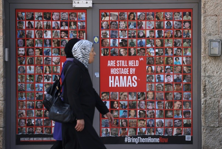 Palestinians pass a store entrance in Jerusalem displaying portraits of Israelis held hostage by Palestinian militants in Gaza