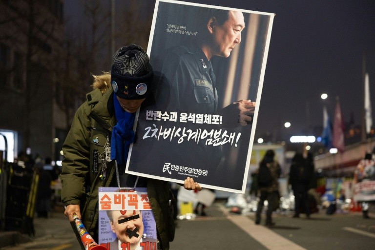 A protester against impeached South Korean President Yoon Suk Yeol walks with placards near the presidential residence